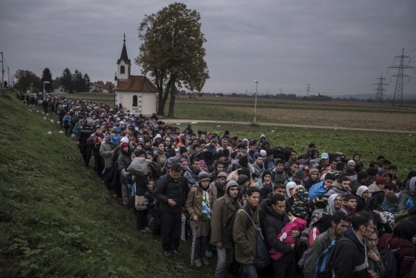 Мигранты, сопровождаемые словенским ОМОНом в регистрационный лагерь, следуют мимо храма