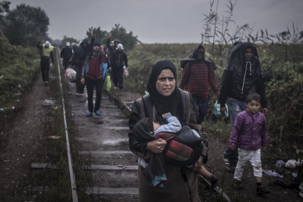 Женщина несет своего ребенка на руках, следуя по железнодорожным путям по направлении к венгерской границе вместе с другими мигрантами