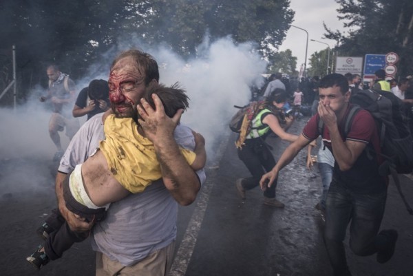 Мужчина пытается защитить сына от ударов и слезоточивого газа во время столкновения мигрантов с венгерской полицией, пытающейся закрыть границу