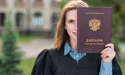 Девушка в мантии выпускника вуза держит в руках диплом о высшем образовании