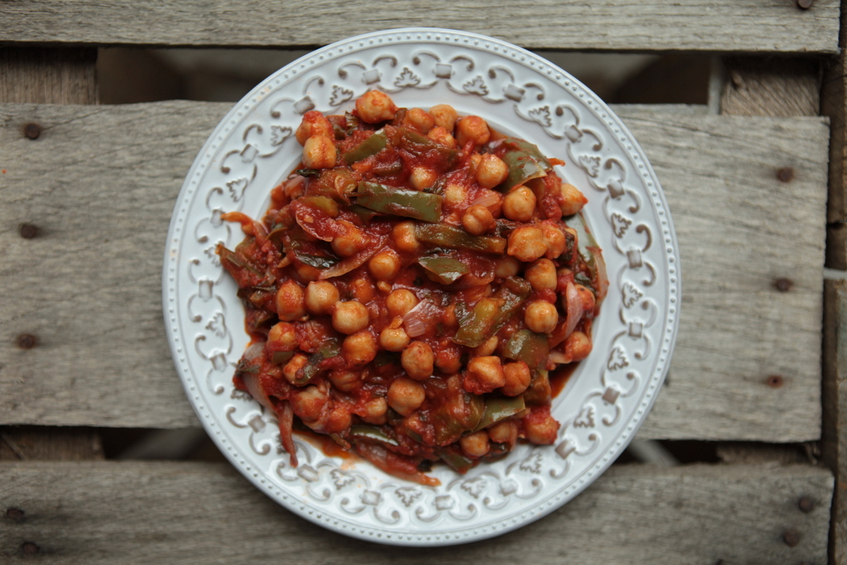 1. Порежьте лук полукольцами, болгарских перец ломтиками, мелко порубите чили. Чеснок раздавите плоской стороной ножа и мелко порежьте. Зелень порежьте. В кастрюле или сотейнике с толстым дном разогрейте на среднем огне оливковое масло. Добавьте болгарский перец, чили, лук, чеснок и готовьте, помешивая, пару минут, пока овощи не станут мягкими.  2. Откройте банки с нутом, жидкость слейте. Отправьте в кастрюлю помидоры и базилик, половину петрушки, приправьте солью и перцем. Накройте крышкой, убавьте температуру и тушите около 5 минут. Затем всыпьте горох нут и тушите еще 5 минут. Такое рагу можно подать с рисом, оно замечательно как холодным, так и горячим. 